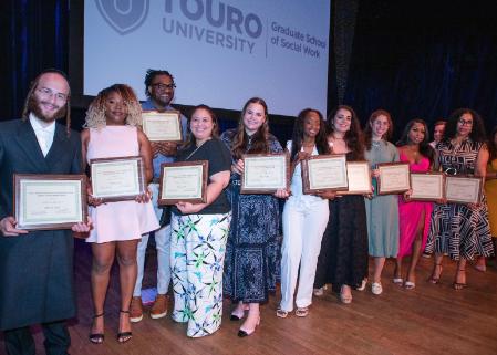 Ten students smile while standing on a stage holding award plaques