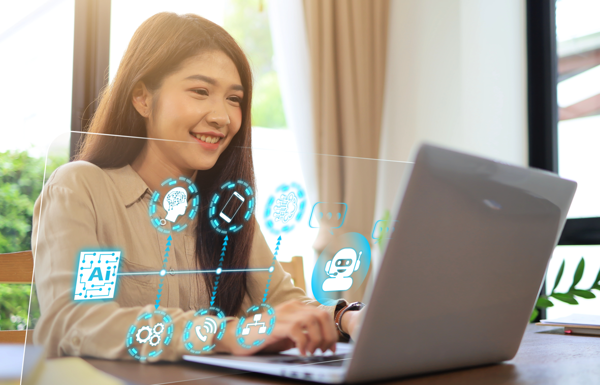 A woman uses a laptop computer by a table. Several holographic images emerge from the laptop. 